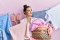 Beautiful brunette young woman holding laundry basket smiling looking to the side and staring away thinking