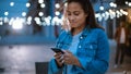 Beautiful Brunette Young Woman is Using a Smartphone while Standing Outdoors in the Evening. She Royalty Free Stock Photo