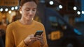 Beautiful Brunette Young Woman is Using a Smartphone while Standing Outdoors in the Evening. She Royalty Free Stock Photo