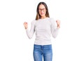 Beautiful brunette young woman wearing casual white sweater and glasses excited for success with arms raised and eyes closed Royalty Free Stock Photo