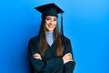 Beautiful brunette young woman wearing graduation cap and ceremony robe happy face smiling with crossed arms looking at the camera Royalty Free Stock Photo