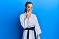 Beautiful brunette young woman wearing karate fighter uniform with black belt bored yawning tired covering mouth with hand Royalty Free Stock Photo