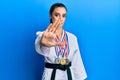 Beautiful brunette young woman wearing karate fighter uniform and medals with open hand doing stop sign with serious and confident