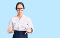 Beautiful brunette young woman wearing professional waitress apron pointing down looking sad and upset, indicating direction with