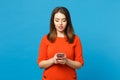 Beautiful brunette young woman wearing red orange dress messaging using mobile phone isolated over trendy blue wall Royalty Free Stock Photo