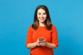 Beautiful brunette young woman wearing red orange dress messaging using mobile phone isolated over trendy blue wall Royalty Free Stock Photo