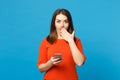 Beautiful brunette young woman wearing red orange dress messaging using mobile phone isolated over trendy blue wall Royalty Free Stock Photo