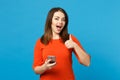 Beautiful brunette young woman wearing red orange dress messaging using mobile phone isolated over trendy blue wall Royalty Free Stock Photo