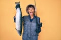 Beautiful brunettte fisher woman holding fishing rod and raw salmon celebrating crazy and amazed for success with open eyes Royalty Free Stock Photo