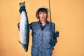 Beautiful brunettte fisher woman holding fishing rod and raw salmon clueless and confused expression Royalty Free Stock Photo