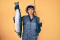 Beautiful brunettte fisher woman holding fishing rod and raw salmon relaxed with serious expression on face Royalty Free Stock Photo