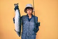 Beautiful brunettte fisher woman holding fishing rod and raw salmon skeptic and nervous, frowning upset because of problem Royalty Free Stock Photo