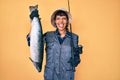 Beautiful brunettte fisher woman holding fishing rod and raw salmon sticking tongue out happy with funny expression Royalty Free Stock Photo