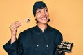 Beautiful brunettte woman chef holding sushi using chopsticks smiling looking to the side and staring away thinking Royalty Free Stock Photo