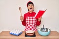 Beautiful brunettte woman cooking cake reading recipes book angry and mad screaming frustrated and furious, shouting with anger