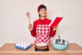 Beautiful brunettte woman cooking cake reading recipes book smiling looking to the side and staring away thinking Royalty Free Stock Photo