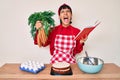 Beautiful brunettte woman cooking carrot cake reading recipes book angry and mad screaming frustrated and furious, shouting with Royalty Free Stock Photo