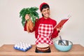 Beautiful brunettte woman cooking carrot cake reading recipes book winking looking at the camera with sexy expression, cheerful Royalty Free Stock Photo