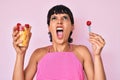 Beautiful brunettte woman eating fresh and healthy fruit angry and mad screaming frustrated and furious, shouting with anger Royalty Free Stock Photo