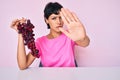 Beautiful brunettte woman holding branch of fresh grapes with open hand doing stop sign with serious and confident expression, Royalty Free Stock Photo