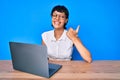 Beautiful brunettte woman working using computer laptop pointing thumb up to the side smiling happy with open mouth Royalty Free Stock Photo