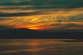 Beautiful burning cloudy sunset at the lake with sun gone behind the mountains