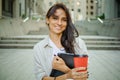 Beautiful business woman is going to work with coffee walking near office buildings. Portrait of a successful business woman holdi Royalty Free Stock Photo