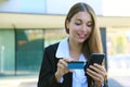 Beautiful business woman holds modern cell phone and credit card making shopping online outdoor office on break time. People and Royalty Free Stock Photo