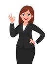 Beautiful business woman showing / gesturing okay / OK sign. Woman in formal black suit isolated white background.