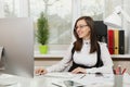 Beautiful business woman in suit and glasses working at computer with documents in light office Royalty Free Stock Photo
