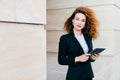 Beautiful businesswoman with curly fluffy hair, wearing elegant clothes, holding tablet in hands, waiting for her business partner Royalty Free Stock Photo