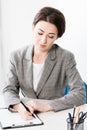 Beautiful businesswoman in grey suit writing something to clipboard Royalty Free Stock Photo