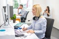 Beautiful businesswoman with headset taking notes to notebook at office desk Royalty Free Stock Photo