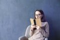 Beautiful businesswoman sitting in loft office reading vintage book. Look into opened book brown cover. Dark blue wall background