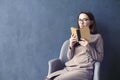 Beautiful businesswoman sitting in loft office reading vintage book. Opened book brown cover. Dark blue wall background, day light