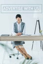 beautiful businesswoman sitting at table and looking at camera on gray with advertise