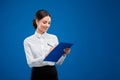 Beautiful businesswoman smiling and writing a new idea on her blue clipboard,  on blue background Royalty Free Stock Photo