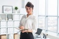 Beautiful businesswoman standing in office, holding notebook, planning meetings for the work day, looking at camera. Royalty Free Stock Photo