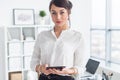 Beautiful businesswoman standing in office, holding notebook, planning meetings for the work day, looking at camera. Royalty Free Stock Photo