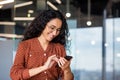 Beautiful businesswoman using phone at workplace, successful and joyful latin american woman typing text message using Royalty Free Stock Photo