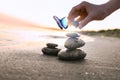 Beautiful butterfly and woman stacking stones on sand near sea at sunset, closeup. Zen concept