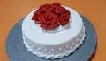 Beautiful cake is covered with white sugarpaste and decorated with red roses