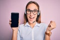 Beautiful call center agent woman working using headset holding smartphone holding screen screaming proud and celebrating victory Royalty Free Stock Photo