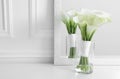 Beautiful calla lily flowers tied with ribbon in glass vase on white table, space for text Royalty Free Stock Photo