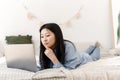 Beautiful calm asian female freelancer is working on a laptop while lying on the bed. Korean young woman doing online Royalty Free Stock Photo