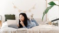 Beautiful calm asian female freelancer is working on a laptop while lying on the bed. Korean young woman doing online Royalty Free Stock Photo