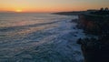 Beautiful calm coastal sunset over foamy ocean splashing on rocky shore aerial Royalty Free Stock Photo