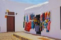 Beautiful calm empty alley, clothing boutique, hanging traditional colorful clothes, flawless bright white typical walls, blue