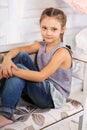 Beautiful calm smiling kid girl sitting on the bench in blue jeans and fashion blouse looking happy. Soft studio portrait Royalty Free Stock Photo