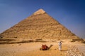 Beautiful camel sitting near the pyramid of Khafre and a walking man nearby, Giza  Cairo, Egypt Royalty Free Stock Photo